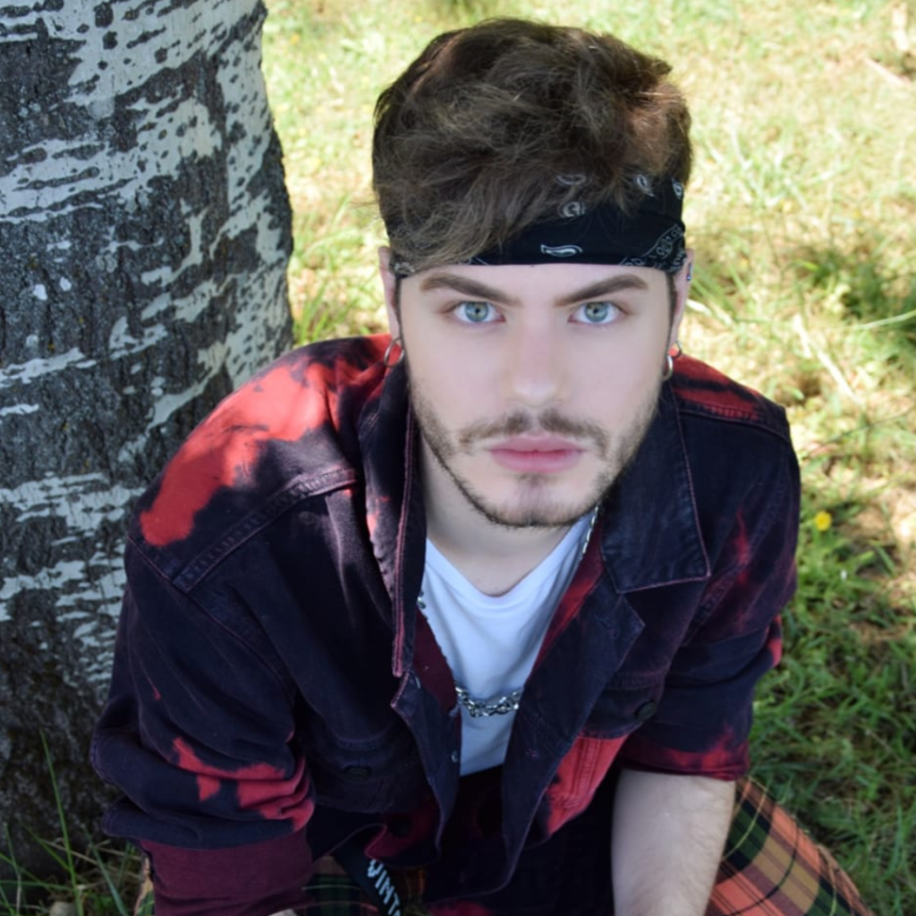 Luca Gremita in una foto a metà figura, ripreso dall'alto: indossa una fascia nera per capelli, una giacca nera e rossa e una maglietta bianca.