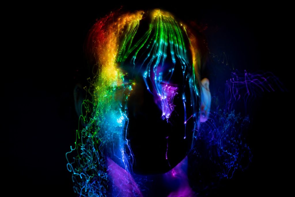 Primo piano di una persona in un ambiente buio: sulla sua faccia passano delle luci arcobaleno.